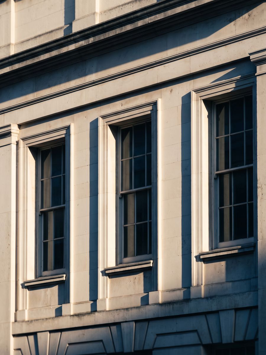 A Portland stone facade in raking afternoon light, its window reveals casting long shadows.
